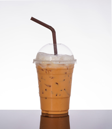 Iced milk tea in takeaway glass, topped with milk foam, on white background and black glass floor.