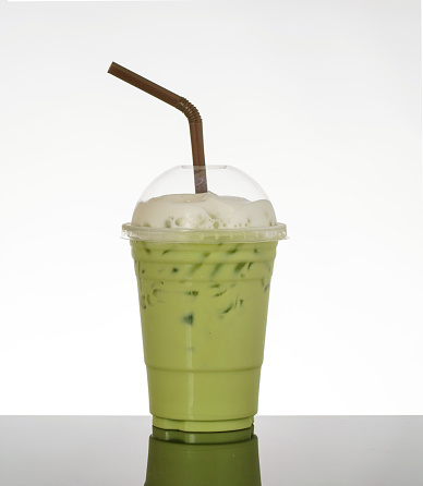 Green tea with milk, topped with frothed milk, on white background and black glass floor.