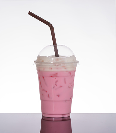 Pink milk, sala flavor, topped with milk foam, on white background and black glass floor.