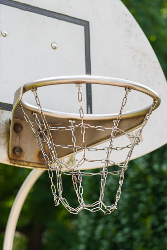 A basketball hoop with a metal chain basket on outdoor playground with summer green trees for street leisure game