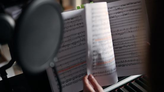Close-up of a person turning the pages of a music sheet. Focus on the piano score book. Blurred foreground.
