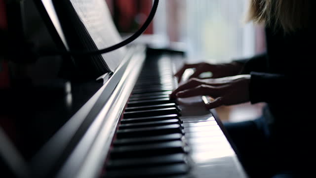 Close-up side-view Woman playing piano. Hands pressing the piano keys. Reading sheet music. Piano learning lessons