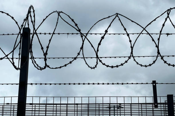 security concept with razor wire fence and camera against stormy sky - razor wire imagens e fotografias de stock