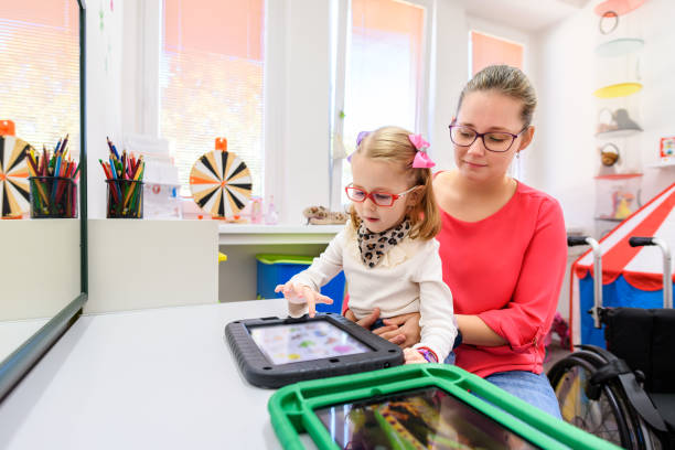 nonverbales mädchen, das mit zerebralparese lebt und lernt, digitale tablet-geräte zur kommunikation zu verwenden. menschen, die schwierigkeiten haben, sprache zu entwickeln oder sprache zu verwenden, verwenden spracherzeugungsgeräte. - child speech therapy adult stock-fotos und bilder