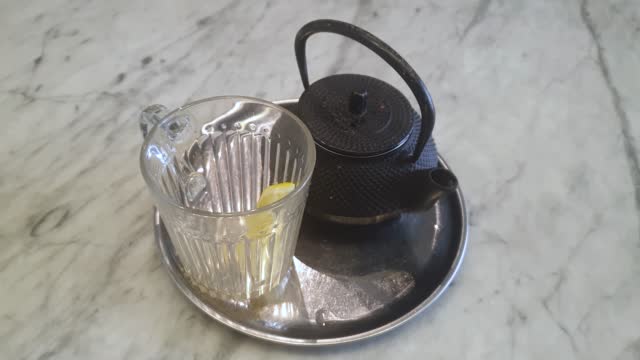 Lemon slice swims in a black tea in a glass tea cup on a table