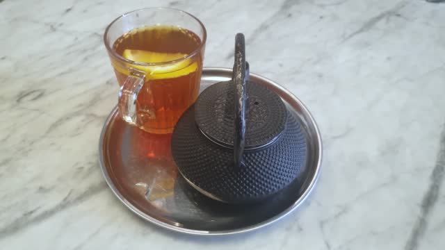 Lemon slice swims in a black tea in a glass tea cup on a table