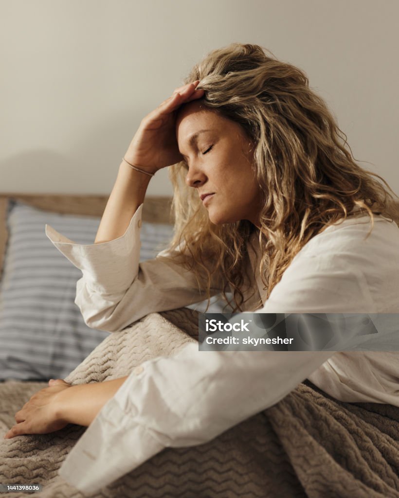 Ugh, I have a headache! Young woman holding her head in pain while relaxing on a bed. Adult Stock Photo