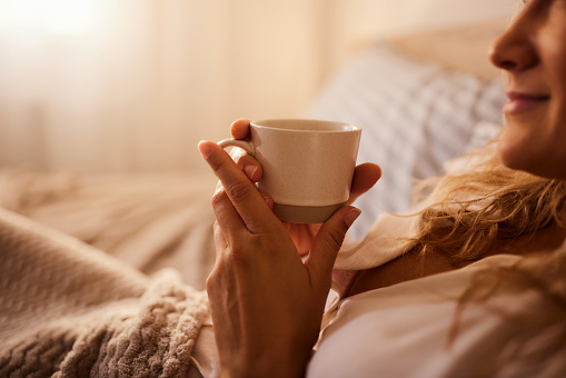Close up of a woman enjoying during coffee time in bed. Copy space.