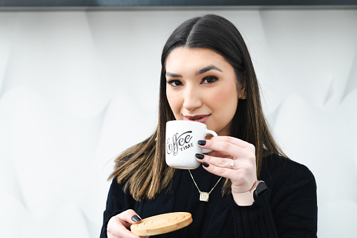 Young beautiful woman drinking coffee while looking at camera in a front view