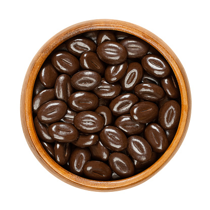 Dark chocolate mocha beans, in a wooden bowl. Candies made of a mixture of coffee bean flavor with indulgent dark chocolate, in the shape of coffee beans. Used as a decoration or as a little snack.