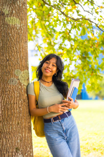 istock Asian girl on campus, smiling at university under tree with block in hand 1441399594