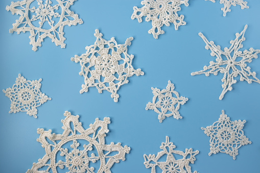 Top view of handmade white crochet snowflakes on blue background. Merry Christmas and happy new year concept.