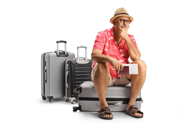 Mature male toruist sitting on a suitcase and waiting for a delayed flight stock photo