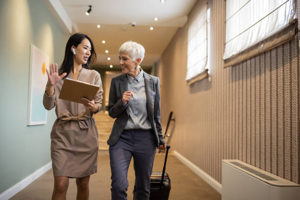 Businesswoman and her assistant checking schedule in hotel corridor Businesswoman and her assistant checking schedule in hotel corridor walking aide stock pictures, royalty-free photos & images