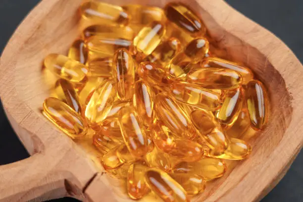 Omega 3 fish oil gold capsules in wooden rustic bowl close up