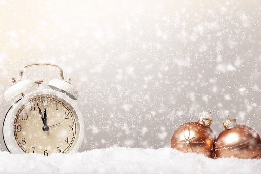 Postcard Merry Christmas. Alarm clock and bauble balls on snow and defocused snowfall.