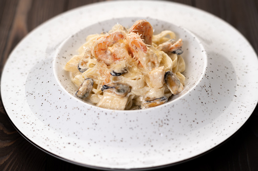 Fettuccine pasta in a creamy sauce with seafood in a plate on a gray concrete background. Pasta with prawns and mussels. Top view, flat lay. Banner