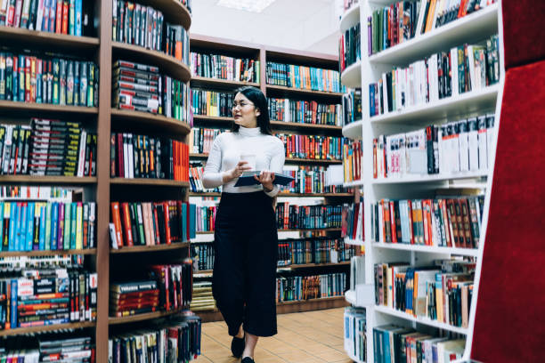 istock Young female walking with coffee in book shop 1441409405
