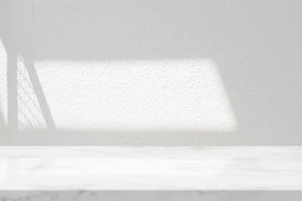 istock White Marble Table with Stucco Wall Texture Background with Light Beam and Fence Shadow, Suitable for Product Presentation Backdrop, Display, and Mock up. 1441409439