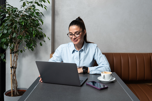 Young business woman freelancer financial expert using her lunch and coffee break to talk about work with his happy satisfied client on video call on laptop. Businessperson conversation office team