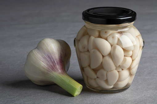 Pickled garlic in a glass jar and a fresh garlic bulb close up
