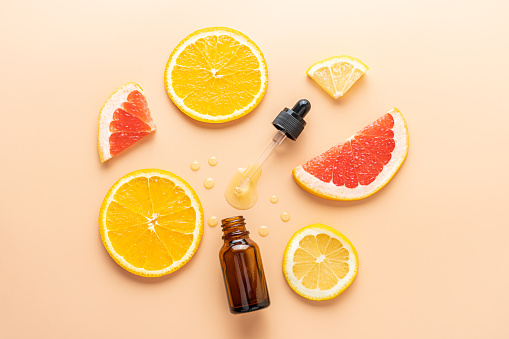 Slice of grapefruit, orange, lemon and serum dropper bottle on beige background, top view