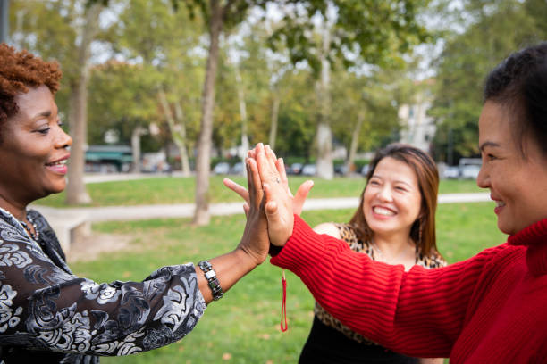 istock Three mature women with joined hands smiling in a public park. 1441412671