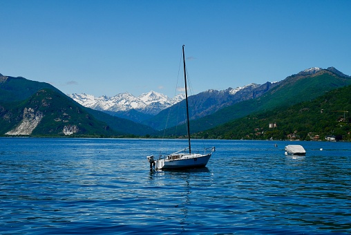 Sailing boat on lake Maggiore with snowy mountains in the background. Piedmont, Italy.