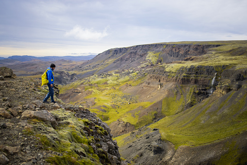 Unrecognizable tourist hiking on the rocky cliff above a stream passing through the rocky terrain on Iceland