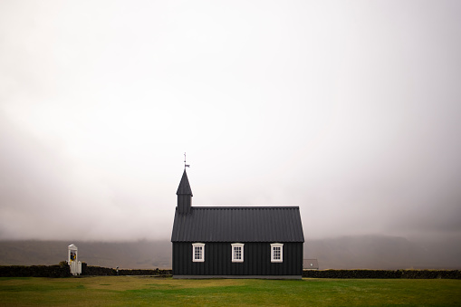Small modest black church on a flat grassy land surrounded by clouds on Iceland