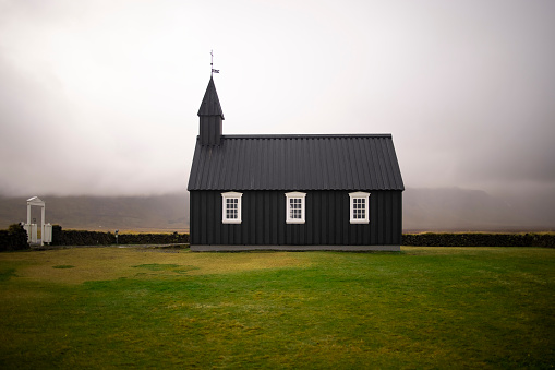 Small modest black church on a flat grassy land surrounded by clouds on Iceland