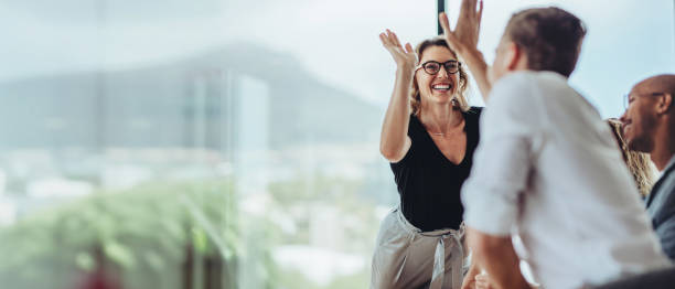 mujer de negocios dando un cinco alto a un colega en la reunión - alegre fotografías e imágenes de stock