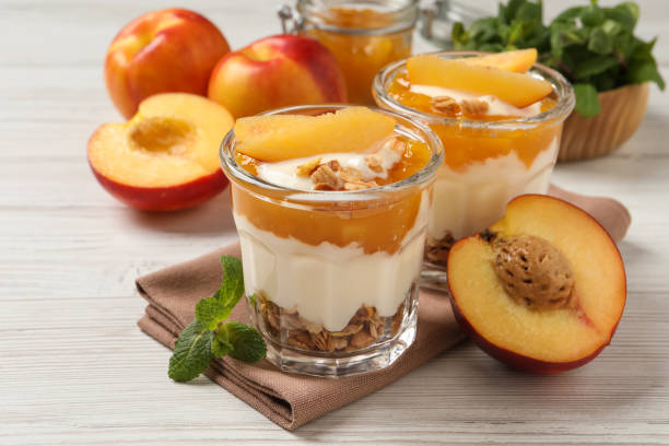 leckerer pfirsichjoghurt mit müsli, obststücken und marmelade auf weißem holztisch - peach nectarine fruit portion stock-fotos und bilder