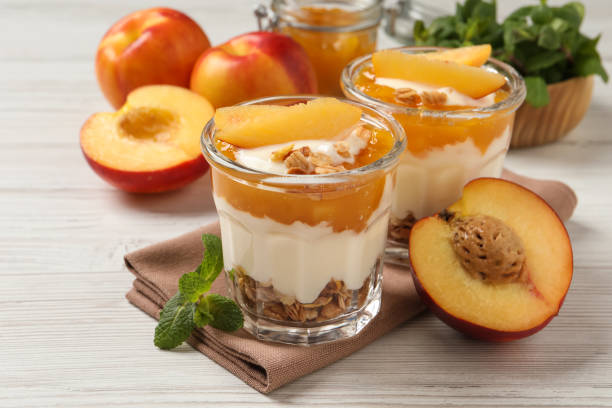 sabroso yogur de melocotón con granola, trozos de fruta y mermelada sobre mesa de madera blanca - peach nectarine portion fruit fotografías e imágenes de stock