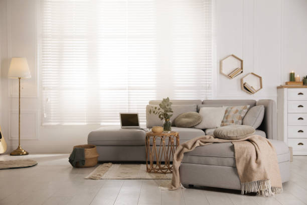Living room with comfortable grey sofa, ottoman and stylish interior elements near window
