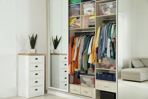 Wardrobe closet with different stylish clothes and home stuff in room. Fast fashion