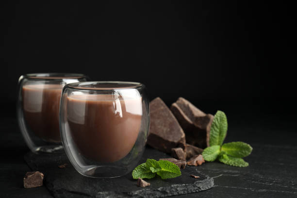 istock Glasses of delicious hot chocolate, chunks and fresh mint on black table. Space for text 1441417780