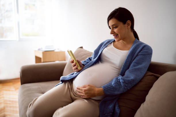 istock Pregnant young woman using phone while relaxing on the sofa at home 1441417944