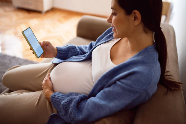 istock Pregnant young woman using phone while relaxing on the sofa at home 1441418381