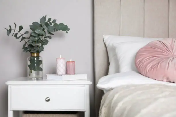 Vase with beautiful eucalyptus branches, book and candles on nightstand in bedroom