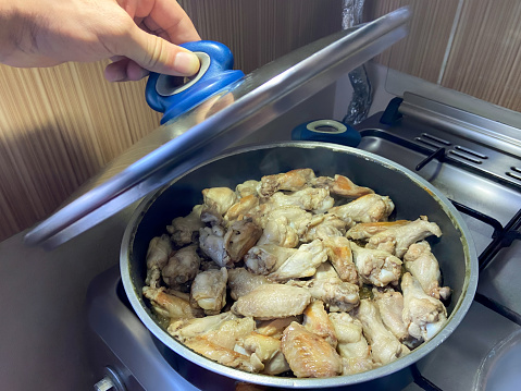 Cooking chicken wings on the burner stove top, chicken wings in the cooking pan and hand opening cooking pan lid