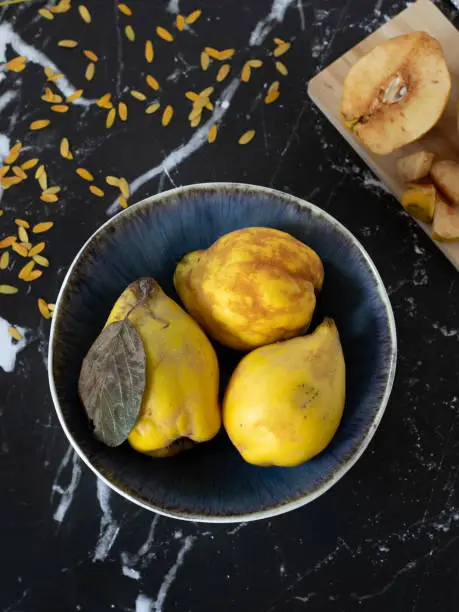 Yellow quince fruit in a bowl on dark background with wooden cutting board and golden autumn leaves. Vertical shot. Top table view.