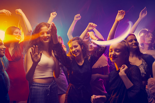 Group of young people, boys and girls attending party, dancing, having fun over dark background in neon light. Celebration. Concept of youth culture, leisure time activity, fun, lifestyle