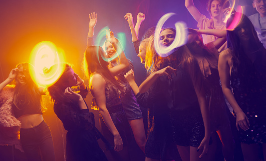 Group of young people, girls and boys, attending party, dancing, having fun over dark background in neon with mixed light. Birthday. Concept of youth culture, leisure time activity, fun, lifestyle