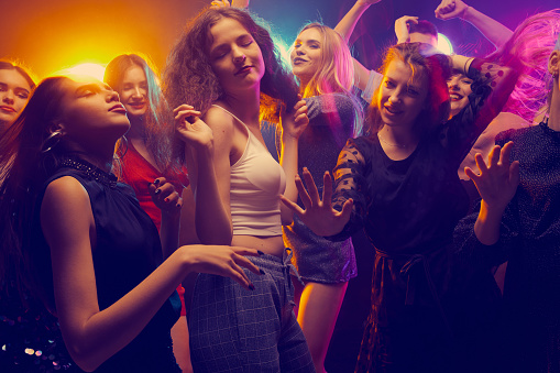 Group of young beautiful people, boys and girls, attending party, dancing, having fun over dark background in neon light. New year celebration. Concept of youth culture, leisure time, fun, lifestyle