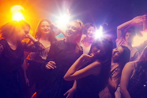 Group of young people attending party, dancing, having fun over dark background in neon light. Birthday surprise. Concept of youth culture, leisure time activity, fun, lifestyle