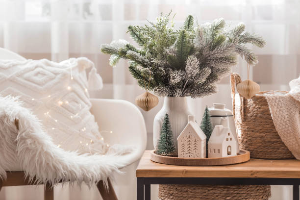 A bouquet of fir trees, a plaid in a wicker basket and Scandinavian white houses on a wooden table in the home interior of the living room. A cozy concept of festive home decoration. New Year's banner, flyer. The concept of New Year and Christmas holidays 2023. florida christmas stock pictures, royalty-free photos & images