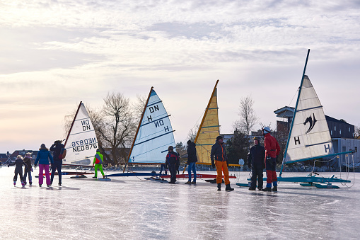 Ice sailing and ice skating on the Braassemermeer near Roelofarendsveen in the municipality of Kaag en Braassem mede Veendermolen on a sunny day. It is mid-February 2021 in the Netherlands, people are skating and ice sailing on a large lake.