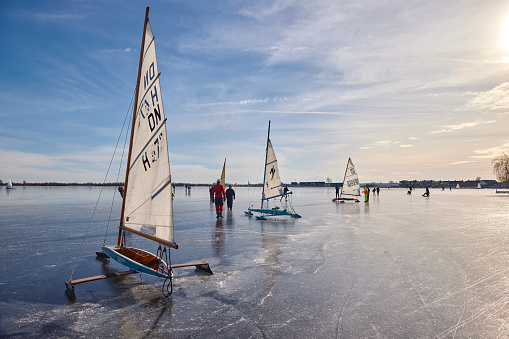 Ice sailing and ice skating on the Braassemermeer near Roelofarendsveen in the municipality of Kaag en Braassem mede Veendermolen on a sunny day. It is mid-February 2021 in the Netherlands, people are skating and ice sailing on a large lake.