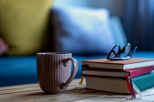 A stack of books and glasses on top of a table next to a mug of tea